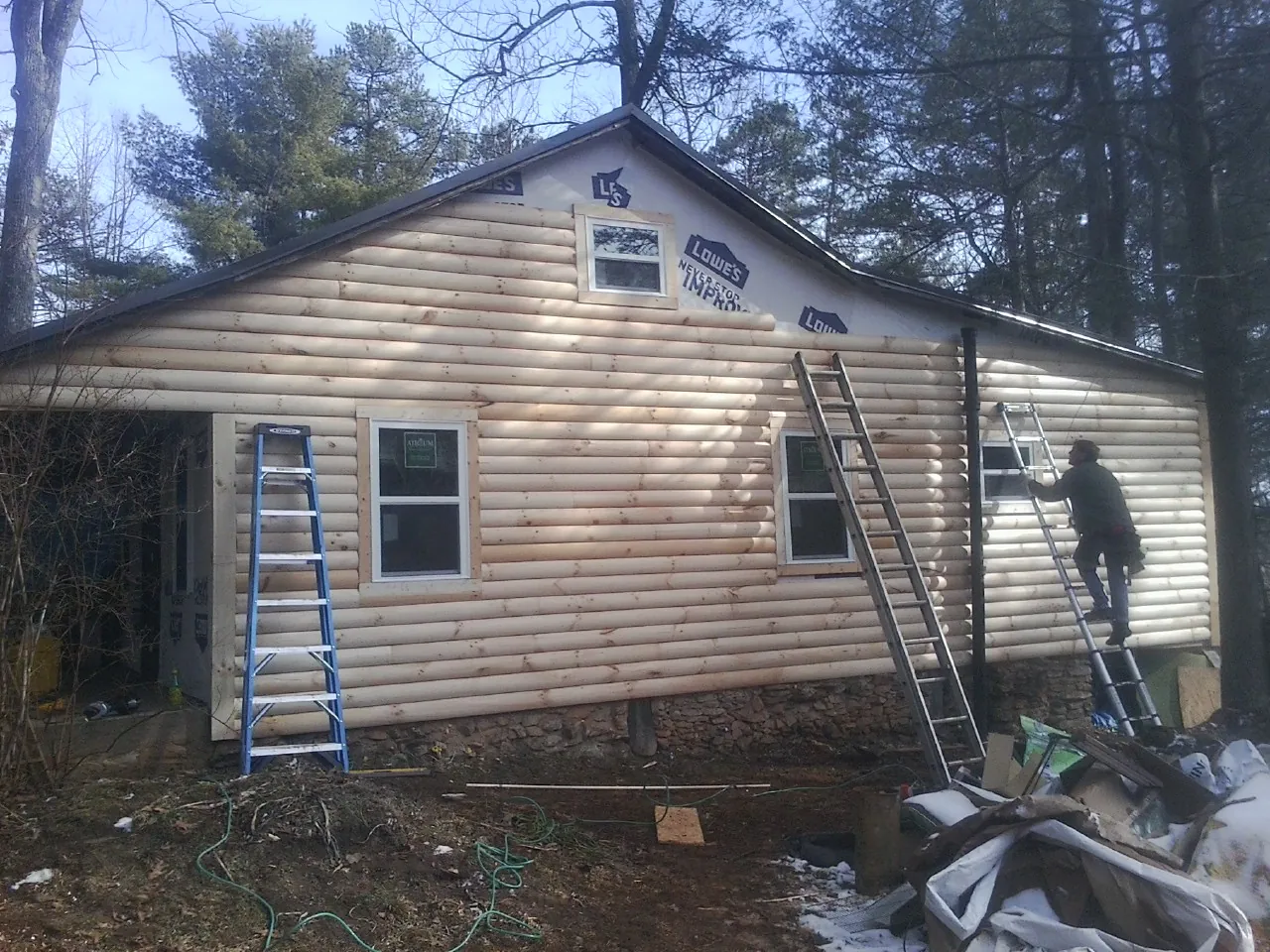 Ladders set against fresh log siding during an exterior remodel in New Ross
