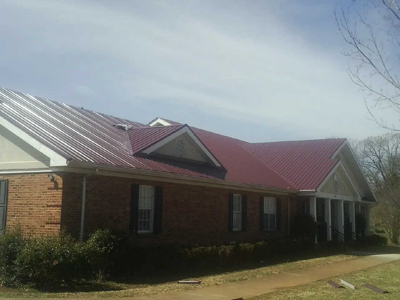 Red metal roof with gabled entries on a long brick building, from a Hail Damage Roof Repair job in New Ross