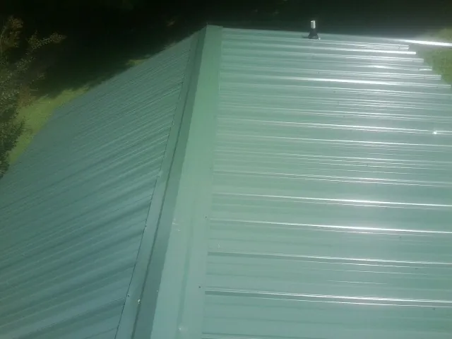 New green metal panels meeting at the ridge of a roof — Flat Roof Repair work by our crew in New Ross