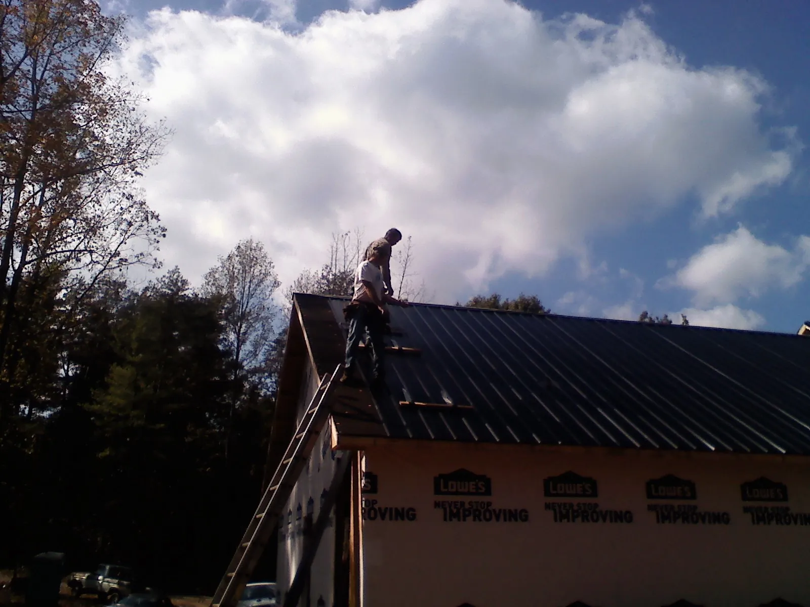 Roofer fastening dark metal panels high against a cloudy sky, from a Roof Inspection job in New Ross