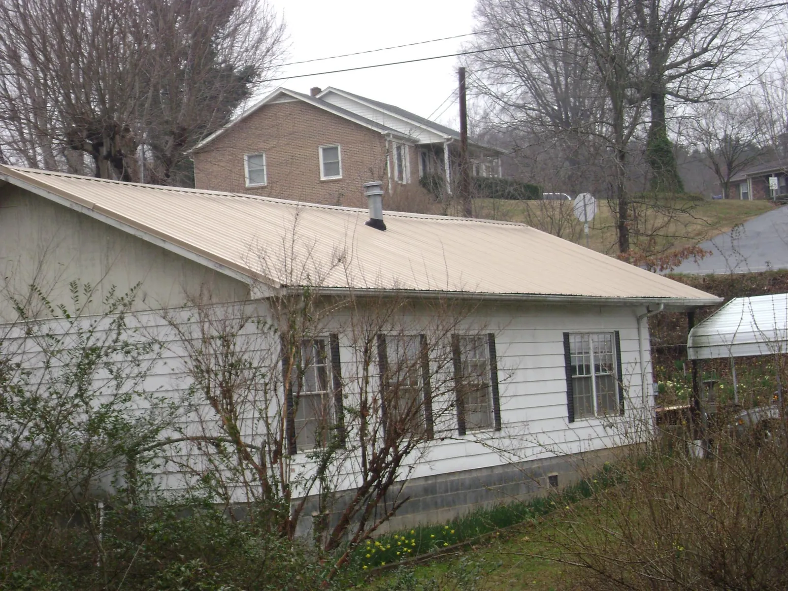 Tan metal roof on a white sided house set into a hillside — Commercial Roofing by Roofing Brothers in New Ross