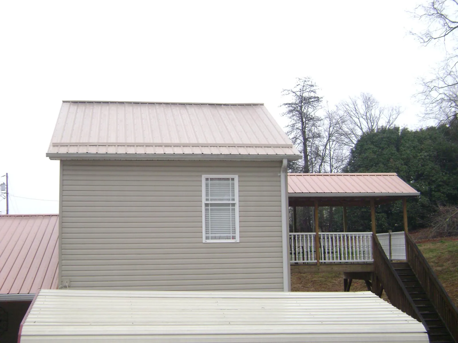 Tan metal roofs on a two story addition and attached porch, from a Roof Replacement job in New Ross